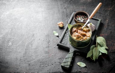 Defne yaprakları ve sarımsak karanfil ile kesme Tahtası üzerinde konserve et bir konserve bir konserve bir konserve açın. Koyu rustik arka plan üzerinde