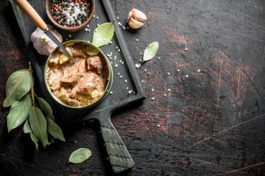 Defne yaprakları ve sarımsak karanfil ile kesme Tahtası üzerinde konserve et bir konserve bir konserve bir konserve açın. Koyu rustik arka plan üzerinde