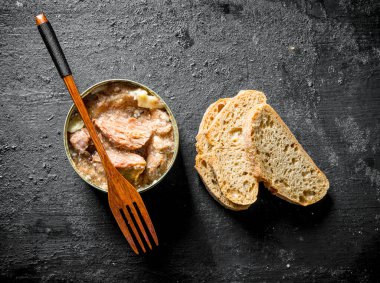Bir çatal ve ekmek dilimleri ile bir konserve et. Siyah rustik arka plan üzerinde