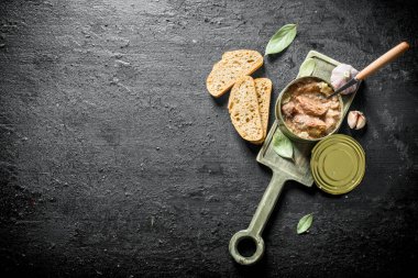 Ekmek ve sarımsak dilimleri ile kesme Tahtası üzerinde bir konserve et. Siyah rustik arka plan üzerinde