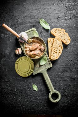 Ekmek ve sarımsak dilimleri ile kesme Tahtası üzerinde bir konserve et. Siyah rustik arka plan üzerinde