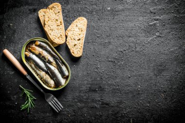 Ekmek ve biberiye dilimleri ile sprats. Siyah rustik arka plan üzerinde