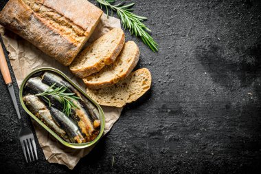 Kağıt üzerinde dilimlenmiş ekmek ile bir tin içinde sprats. Siyah rustik arka plan üzerinde