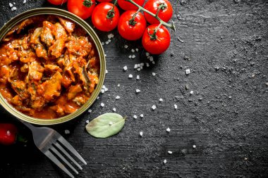 Taze kiraz domates ile bir konserve sprat. Siyah rustik arka plan üzerinde