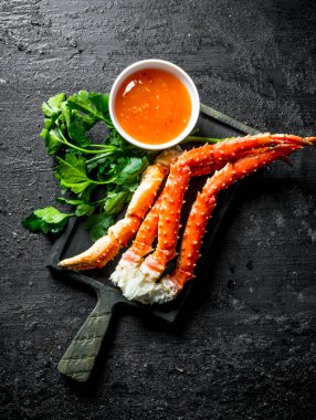 Maydanoz ve soslu kesme tahtasında yengeç. Siyah rustik arka plan üzerinde