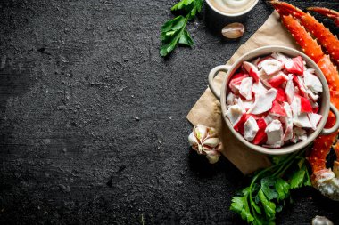 Yeşillik, sos ve sarımsak ile kağıt üzerinde kase de Yengeç eti. Siyah rustik arka plan üzerinde