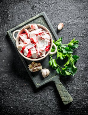 Maydanoz ve sarımsak karanfil ile kesme Tahtası üzerinde bir kapta Yengeç eti. Siyah rustik arka plan üzerinde