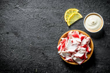 Sos lu ve limon dilimleri olan bir tabakta yengeç eti. Siyah rustik arka plan üzerinde