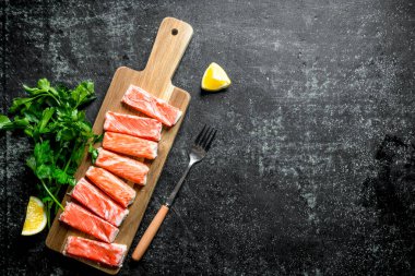 Yengeç maydanoz ve limon ile doğrama tahtası üzerinde sopalarla. Koyu rustik arka plan üzerinde