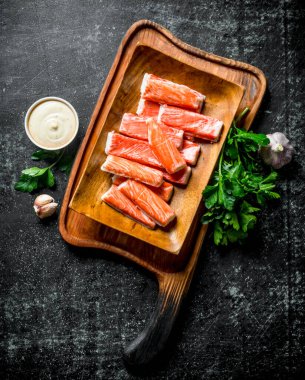 Yengeç yeşillik, sos ve sarımsak ile kesme Tahtası üzerinde sopalarla. Koyu rustik arka plan üzerinde