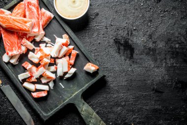 Dilimlenmiş yengeç kesme tahtasına yapışır. Siyah rustik arka plan üzerinde