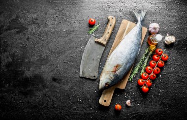 Bir bıçak, domates ve sarımsak ile kesme Tahtası üzerinde çiğ balık. Siyah rustik arka plan üzerinde