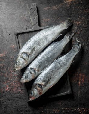 Ahşap kesme Tahtası üzerinde çiğ levrek balık. Koyu rustik arka plan üzerinde