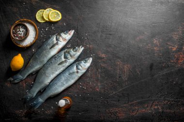 Dilimlenmiş limon ve baharatile çiğ levrek balığı. Koyu rustik arka plan üzerinde
