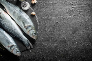 Bir taş Tahta üzerinde sarımsak karanfil ve baharat ile çiğ balık. Siyah rustik arka plan üzerinde