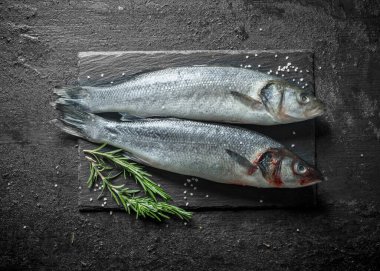 Biberiyeli iki balık çiğ levrek. Siyah rustik arka plan üzerinde