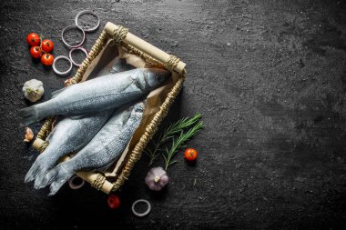 Domates, sarımsak ve soğan halkaları ile bir sepet içinde çiğ balık. Siyah rustik arka plan üzerinde