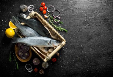 Limon, soğan halkaları ve sarımsak ile bir sepet içinde çiğ balık. Siyah rustik arka plan üzerinde