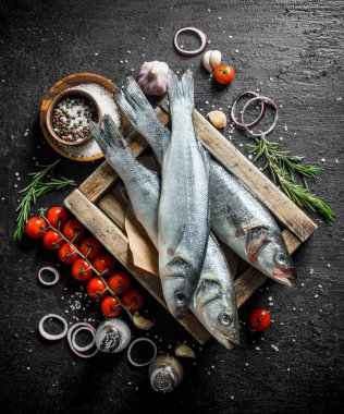 Domates, baharat, sarımsak, biberiye ve soğan halkaları ile ahşap bir tepsi üzerinde Çiğ balık. Siyah rustik arka plan üzerinde