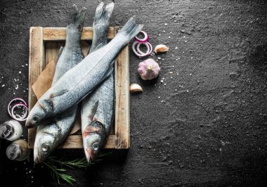 Sarımsak, baharat ve soğan halkaları ile tepside çiğ balık. Siyah rustik arka plan üzerinde