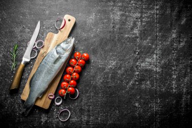 Bıçak, kiraz domates ve soğan halkaları ile Kesme Kurulu çiğ balık. Siyah rustik arka plan üzerinde