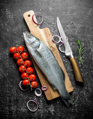 Bıçak, kiraz domates ve soğan halkaları ile Kesme Kurulu çiğ balık. Siyah rustik arka plan üzerinde