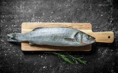 Biberiye ile kesme Kurulu çiğ balık levrek. Koyu rustik arka plan üzerinde