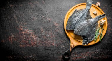 Sarımsak ve biberiye ile ahşap kesme Kurulu çiğ balık pisi balığı. Koyu rustik arka plan üzerinde