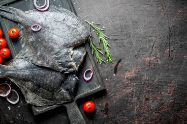 Çiğ balık kiraz domates ve dilimlenmiş soğan ile kesme Kurulu üzerinde flounder. Koyu rustik arka plan üzerinde