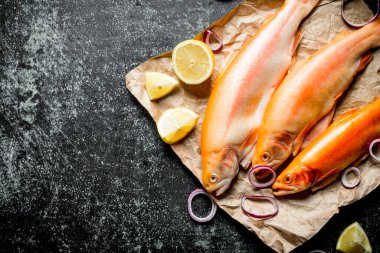 Soğan halkaları ve limon dilimleri ile kağıt üzerinde çiğ alabalık balık. Koyu rustik arka plan üzerinde