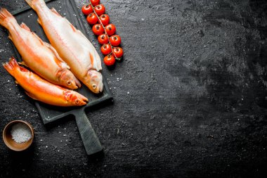 Bir dal ve tuz bir kase domates ile kesme Kurulu çiğ balık alabalık. Siyah rustik arka plan üzerinde