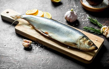 Limon dilimleri, sarımsak ve biberiye ile tuzlu ringa balığı. Koyu rustik arka plan üzerinde