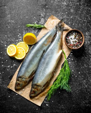 Limon dilimleri, dereotu ve baharatlar ile kağıt üzerinde tuzlu ringa balığı. Koyu rustik arka plan üzerinde