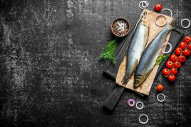 Otlar, domates, soğan halkaları ve baharatlar ile tuzlu ringa balığı. Koyu rustik arka plan üzerinde