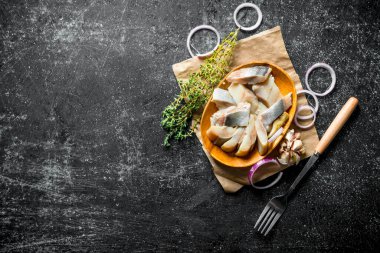 Kekik, sarımsak ve soğan halkaları ile bir tabak tabakta tuzlu ringa fileto. Koyu rustik arka plan üzerinde