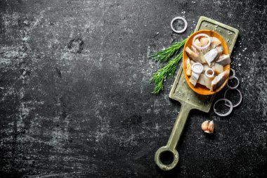 Dereotu, soğan ve sarımsak ile kesme Tahtası üzerinde tuzlu ringa parçaları. Koyu rustik arka plan üzerinde