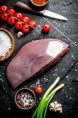 Çiğ karaciğer, çeri domates ve baharatlar. Siyah rustik arka plan üzerinde