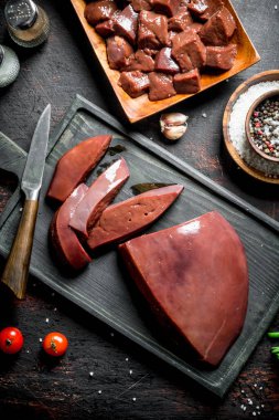 Kesme Tahtasında bıçak olan çiğ karaciğer parçaları. Koyu rustik arka plan üzerinde