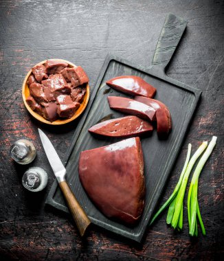 Bir tabakta ve kesme tahtasında çiğ karaciğer parçaları. Koyu rustik arka plan üzerinde