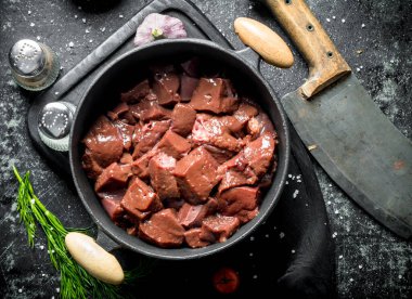 Bıçak, baharat ve dereotu ile bir tencerede dilimlenmiş çiğ karaciğer. Koyu rustik arka plan üzerinde