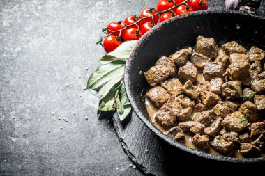 Defne yaprağı ve domates ile bir tavada kızarmış karaciğer. Koyu rustik arka plan üzerinde