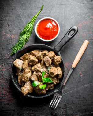 Otlar ve domates sosu ile bir tavada kızartılmış karaciğer parçaları. Koyu rustik arka plan üzerinde