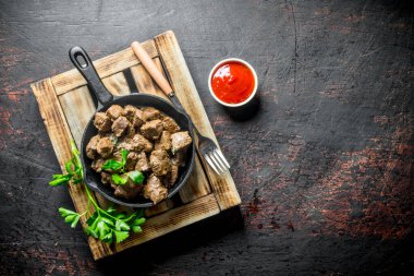 Domates soslu tepside kızarmış karaciğer parçaları. Koyu rustik arka plan üzerinde