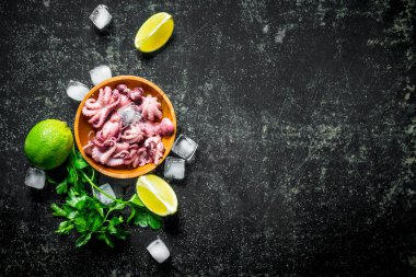 Kireç, buz ve maydanoz dilimleri ile bir tabak üzerinde bebek ahtapot. Koyu rustik arka plan üzerinde