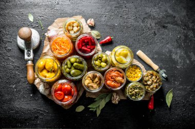 Kağıt üzerinde cam kavanozlarda farklı korunmuş gıda çeşitleri. Siyah rustik arka plan üzerinde