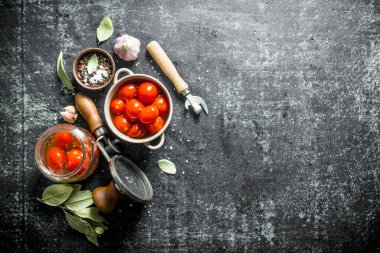 Bir kase ve cam bir kavanozda ev yapımı korunmuş domates. Koyu rustik arka plan üzerinde