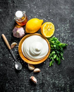 Otlar, sarımsak dilimleri ve limon dilimleri ile bir tabakta mayonez. Koyu rustik arka plan üzerinde