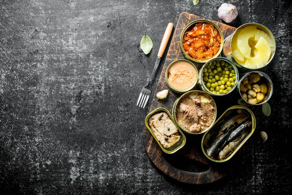 Ahşap kesme Tahtası üzerinde çeşitli konserve gıda ile açık konserve ler. Koyu rustik arka plan üzerinde