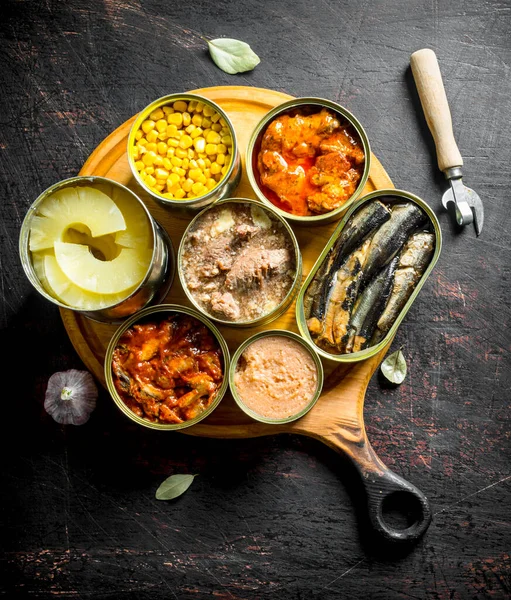 Yuvarlak kesme tahtasında konserve yiyecek. Koyu rustik arka plan üzerinde