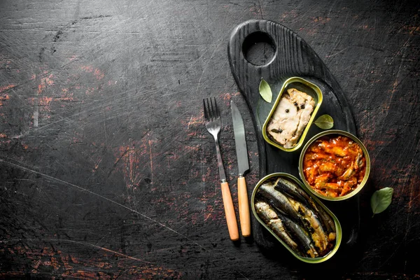 Kesme tahtasında konserve balıklar konserve. Koyu rustik arka plan üzerinde